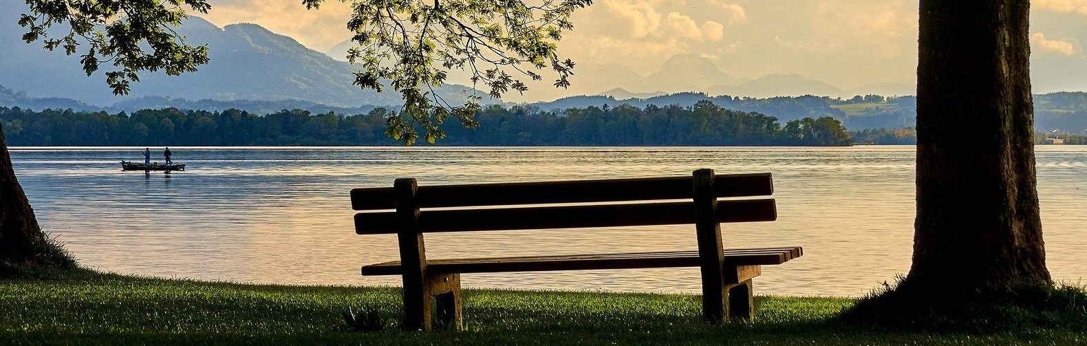 Eine Bank steht vor einem See und die Sonne geht unter.