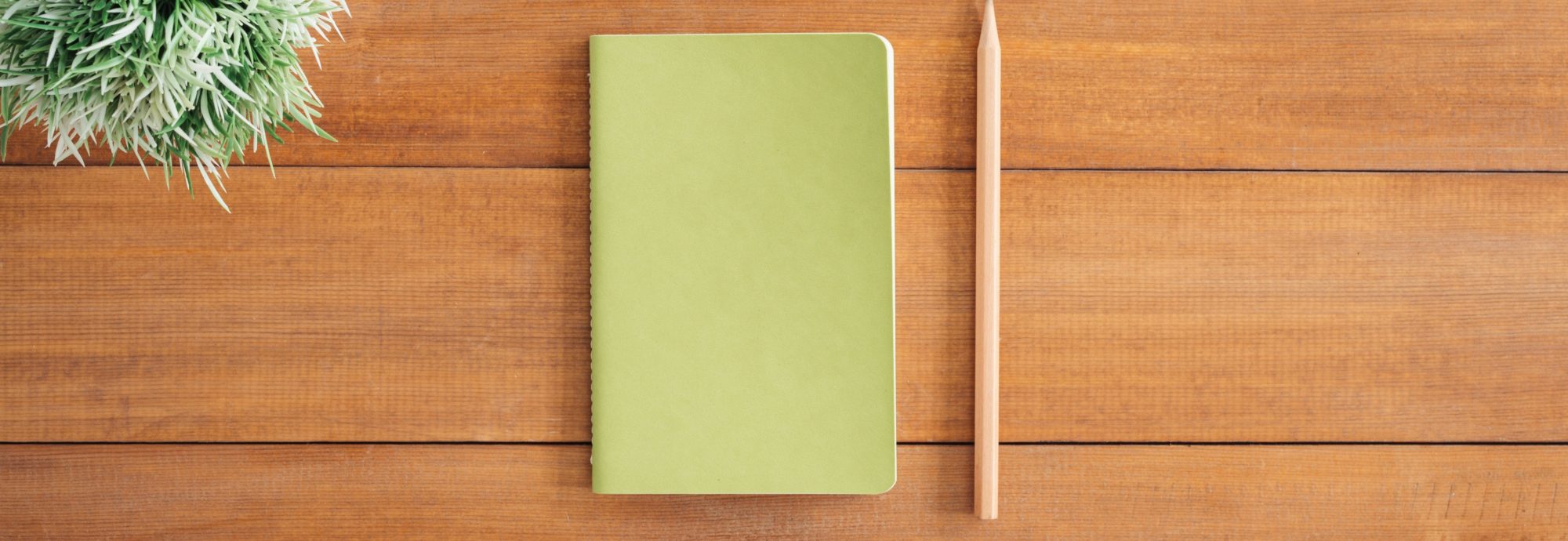 Ein grünes Notizbuch liegt auf einem Holztisch.