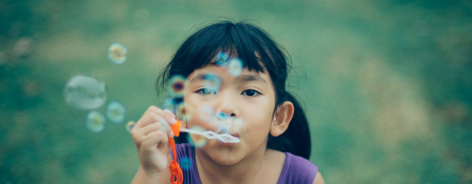 Ein kleines Mädchen pustet Seifenblasen in die Kamera.