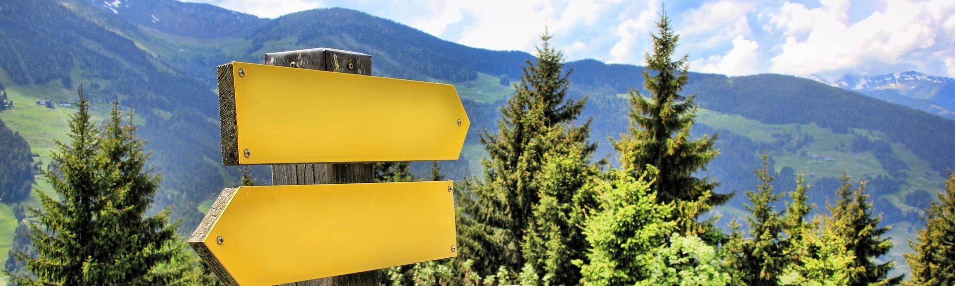 Man sieht zwei Schilder eines Wegweisers in den Bergen.