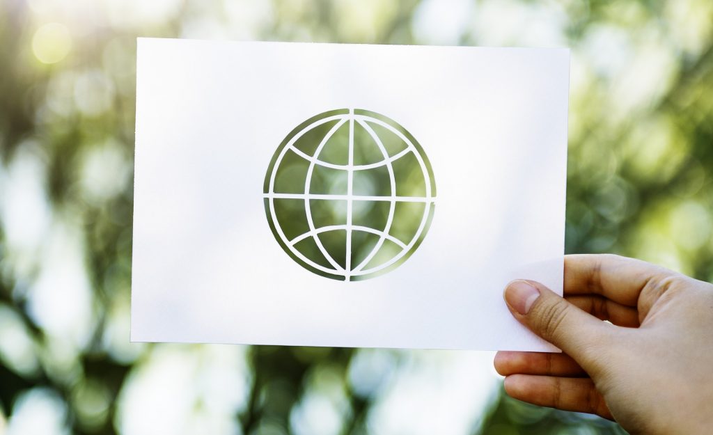 Ein Papier mit ausgeschnittener Weltkugel wird vor einem verschwommenen Hintergrund mit Bäumen gehalten.