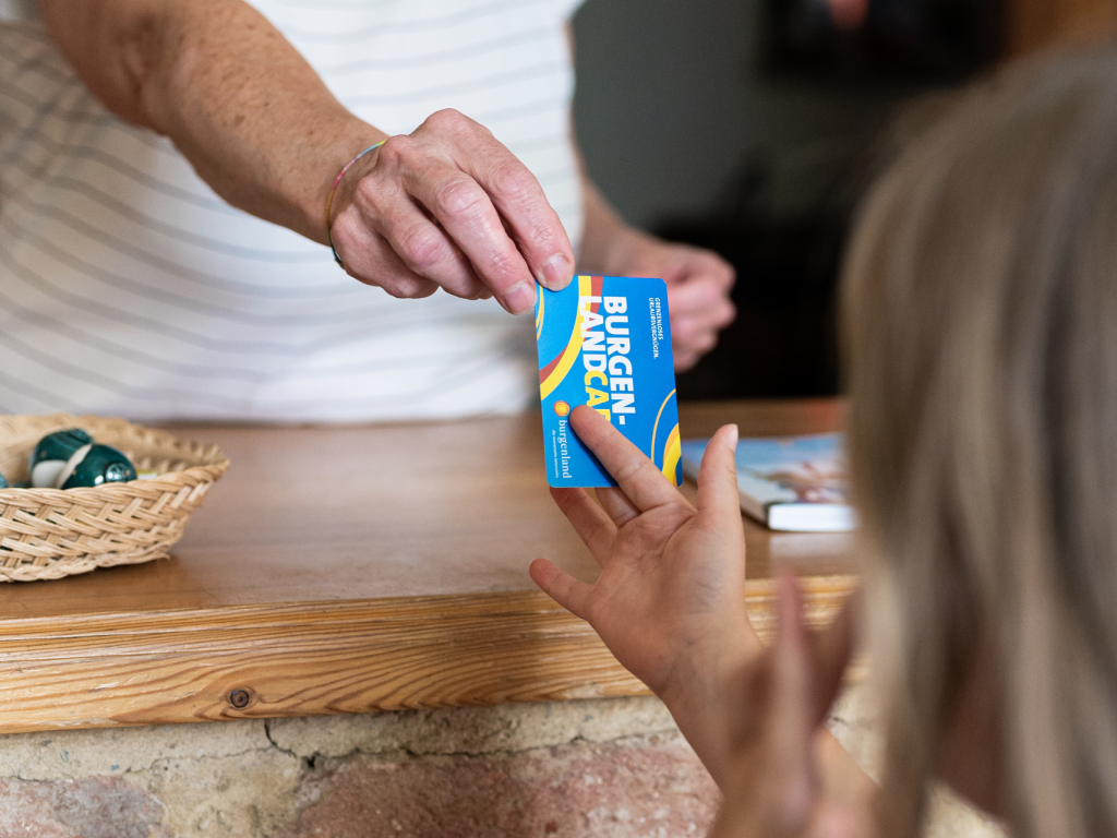 A woman hands a Burgenland Card to a tourist at a stand.